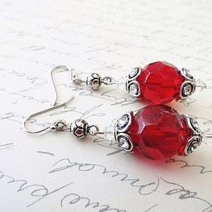 May include: A pair of silver earrings with red faceted glass beads and silver filigree accents.