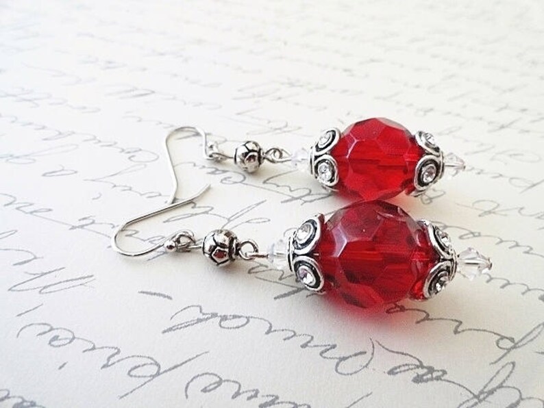 May include: A pair of silver earrings with red faceted glass beads and silver filigree accents.