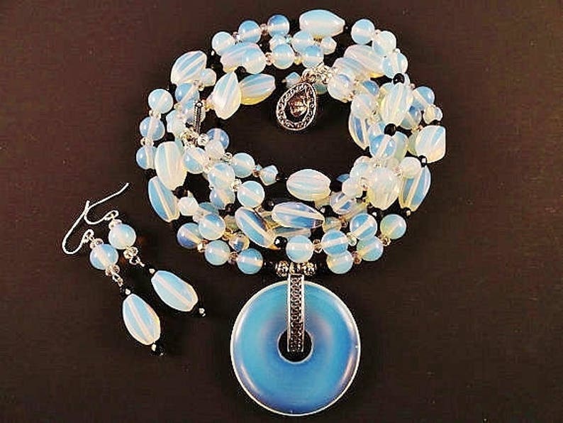 May include: A blue and white opal necklace with a large pendant and matching earrings. The necklace is made of multiple strands of beads and the pendant is a large, round opal.