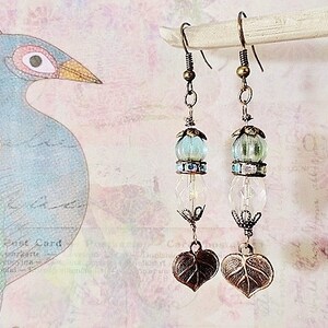 May include: A pair of dangle earrings with a light blue and clear glass bead and a bronze leaf charm.