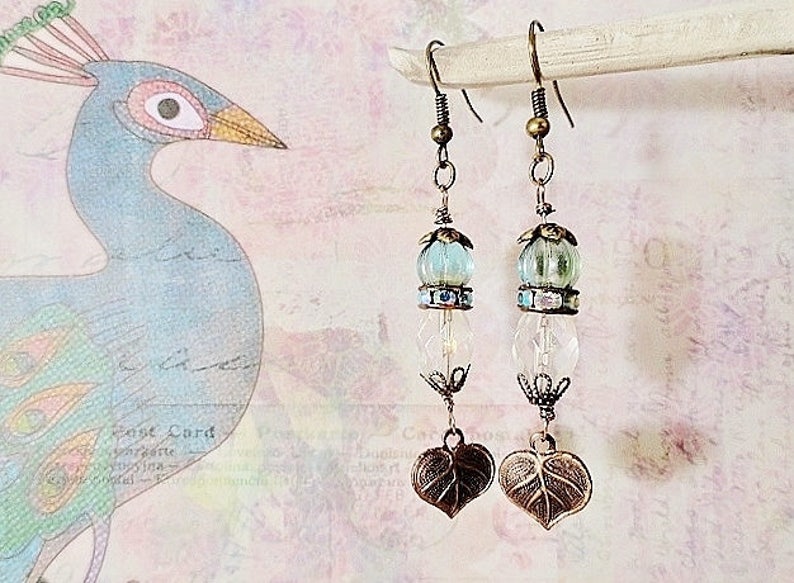 May include: A pair of dangle earrings with a light blue and clear glass bead and a bronze leaf charm.