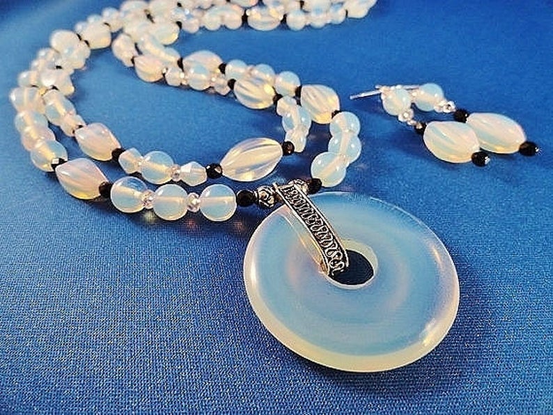 May include: A white opal necklace and earrings set with a silver pendant. The necklace features white opal beads and black beads. The pendant is a round opal with a silver design.