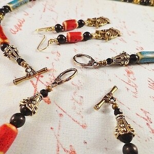 May include: A necklace and earrings set with black, red, and blue ceramic beads, gold-tone metal accents, and black glass beads.