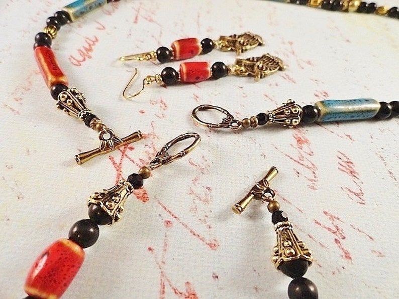May include: A necklace and earrings set with black, red, and blue ceramic beads, gold-tone metal accents, and black glass beads.