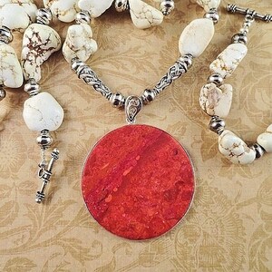 May include: A necklace with a large, round, red coral pendant and white howlite beads. The necklace has a silver chain and silver toggle clasp.