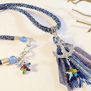 May include: A blue denim necklace with a silver anchor charm and a blue and purple tassel. The necklace also features a silver star charm and blue glass beads.