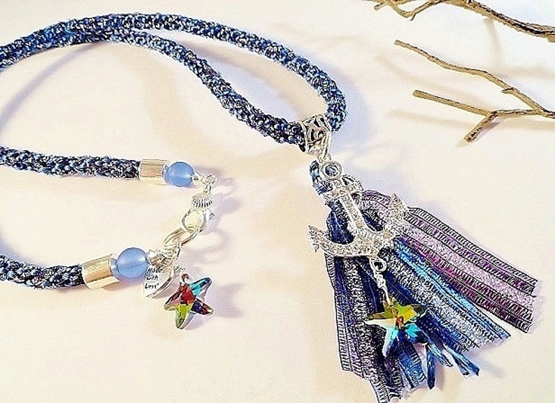 May include: A blue denim necklace with a silver anchor charm and a blue and purple tassel. The necklace also features a silver star charm and blue glass beads.