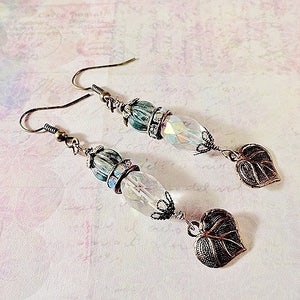 May include: A pair of earrings with a teardrop-shaped crystal bead, a green and blue bead, and a leaf-shaped charm. The earrings are made of silver-toned metal.