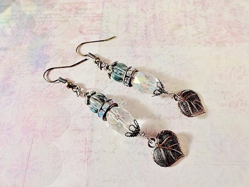 May include: A pair of earrings with a teardrop-shaped crystal bead, a green and blue bead, and a leaf-shaped charm. The earrings are made of silver-toned metal.