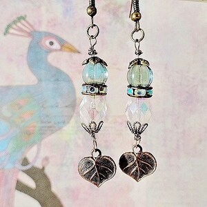 May include: A pair of dangle earrings with a blue and white glass bead, a clear crystal bead, and a leaf-shaped charm. The earrings are made with a bronze-colored metal.