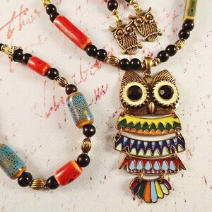 May include: A colorful owl pendant necklace with black and red beads. The owl has a yellow, green, blue, and orange design. The necklace comes with a matching bracelet and a pair of owl earrings.