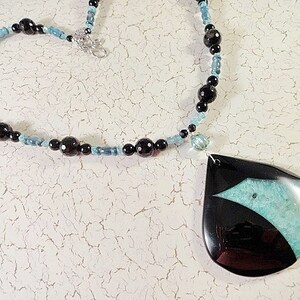 Peut inclure: Un collier avec un pendentif en agate noir et turquoise, composé de perles noires et bleues. Le pendentif a la forme d'une larme et présente un motif en agate noir et turquoise.