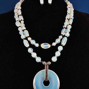 May include: A double-strand necklace with a large, round, light blue pendant. The necklace is made of white and black beads. The pendant has a silver ring in the center.