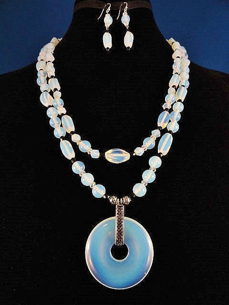 May include: A double-strand necklace with a large, round, light blue pendant. The necklace is made of white and black beads. The pendant has a silver ring in the center.