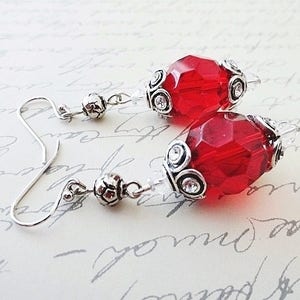 May include: A pair of silver earrings with red faceted glass beads. The beads are accented with silver filigree and small clear rhinestones.