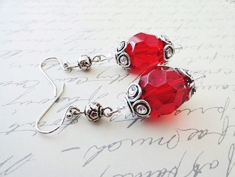 May include: A pair of silver earrings with red faceted glass beads. The beads are accented with silver filigree and small clear rhinestones.