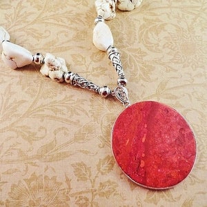 May include: A white howlite stone necklace with a silver chain and a large red coral pendant.