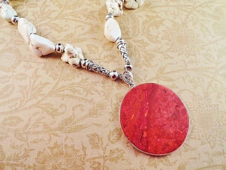 May include: A white howlite stone necklace with a silver chain and a large red coral pendant.