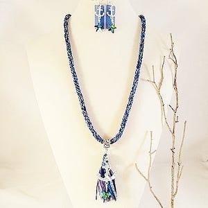 May include: A blue and white braided necklace with an anchor charm and a tassel. The necklace is paired with matching earrings featuring a blue and white anchor charm.