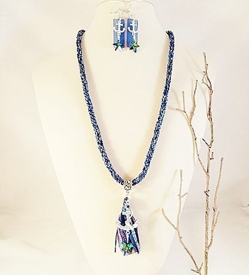 May include: A blue and white braided necklace with an anchor charm and a tassel. The necklace is paired with matching earrings featuring a blue and white anchor charm.