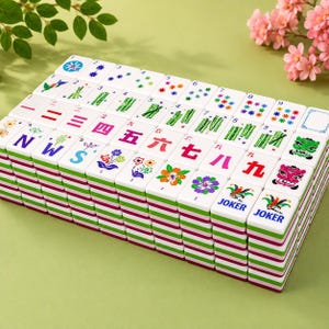 K&ouml;nnte beinhalten: Ein Set aus wei&szlig;en Mahjong-Spielsteinen, die in einem rechteckigen Block angeordnet sind. Die Steine zeigen bunte Illustrationen von Blumen, Bambus, Zahlen und das Wort JOKER. Jeder Stein hat eine geschichtete Basis mit horizontalen Streifen.