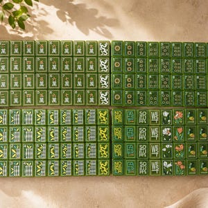 May include: A complete set of green Mahjong tiles arranged in four rectangular blocks. The tiles feature traditional Chinese characters, numeric symbols, bamboo patterns, directional text including North, East, South, West, and floral Joker tiles.