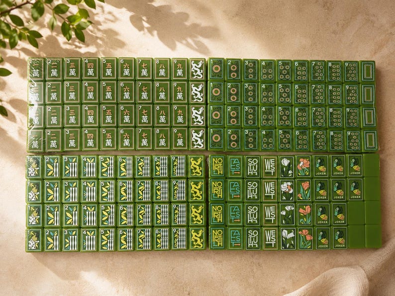 May include: A complete set of green Mahjong tiles arranged in four rectangular blocks. The tiles feature traditional Chinese characters, numeric symbols, bamboo patterns, directional text including North, East, South, West, and floral Joker tiles.