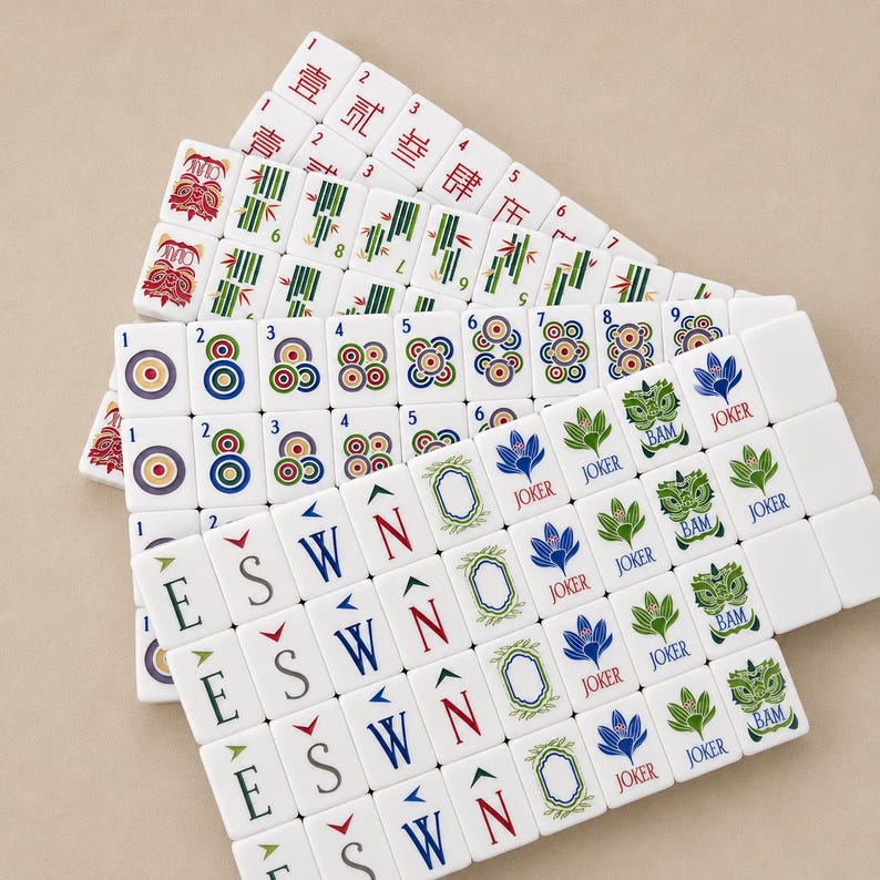 May include: A collection of white Mahjong tiles arranged in overlapping rows. The tiles feature various colorful designs including Chinese characters, bamboo stalks, circular patterns, directional letters E, S, W, N, and illustrations labeled Joker and Bam.