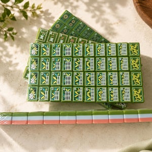 May include: A set of green mahjong tiles arranged in a rectangular grid, featuring bamboo patterns numbered one through nine, dragon symbols, and Chinese characters. A single row of tiles with green, white, and pink edges lies in the foreground.
