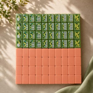 May include: A set of rectangular mahjong tiles arranged in a grid. The top four rows feature green tiles with white, yellow, and black illustrations of bamboo, numbers one through nine, and dragon motifs. The bottom four rows consist of solid peach tiles.