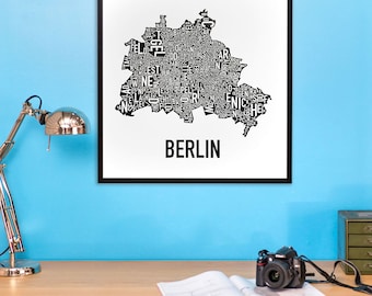Może przedstawiać: Czarno-biała mapa typograficzna Berlina, Niemcy. Mapa jest wydrukowana na białym papierze i oprawiona w czarną ramę. Mapa wisi na jasnoniebieskiej ścianie. Mapa jest otoczona biurkiem z lampą, notesem i aparatem.