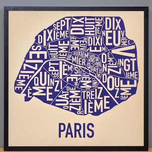 May include: A blue and white typography print of the city of Paris, with the names of the different arrondissements, or districts, of the city. The print is framed in black and set against a cream background.
