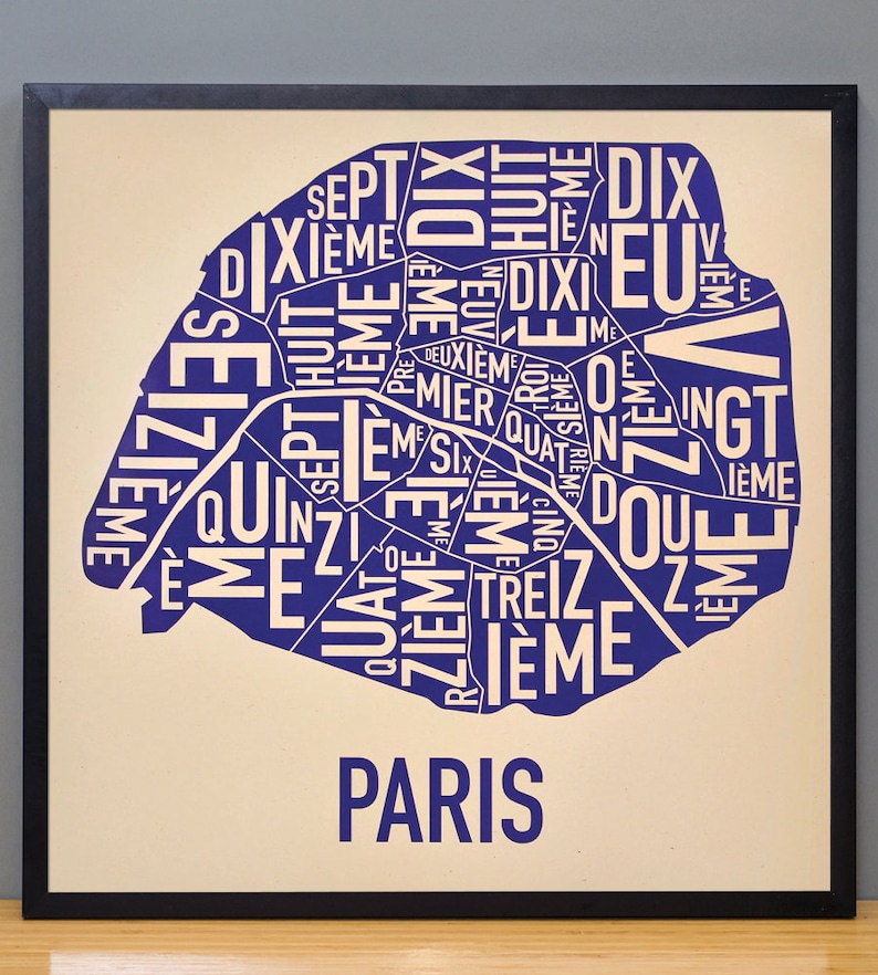 May include: A blue and white typography print of the city of Paris, with the names of the different arrondissements, or districts, of the city. The print is framed in black and set against a cream background.