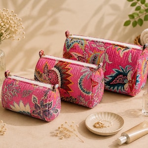 Puede incluir: Tres estuches cilíndricos acolchados de diferentes tamaños, con una base de color rosa vibrante y un estampado floral y de cachemira multicolor. Cada estuche tiene una cremallera blanca en la parte superior, textura acolchada y forma redondeada.