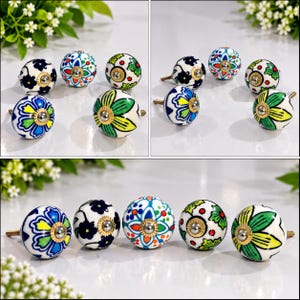 May include: A collection of round ceramic cabinet knobs featuring various hand-painted floral and geometric patterns in vibrant shades of blue, green, red, and yellow, each finished with a central metallic screw and a decorative brass-toned metal base.