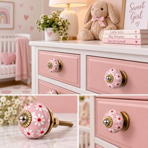 May include: A round ceramic drawer knob featuring a pink background with a repeating white daisy pattern and a red center. The knob has a metallic brass-toned base and a silver-colored center accent, shown installed on pink drawers and as a single unit.