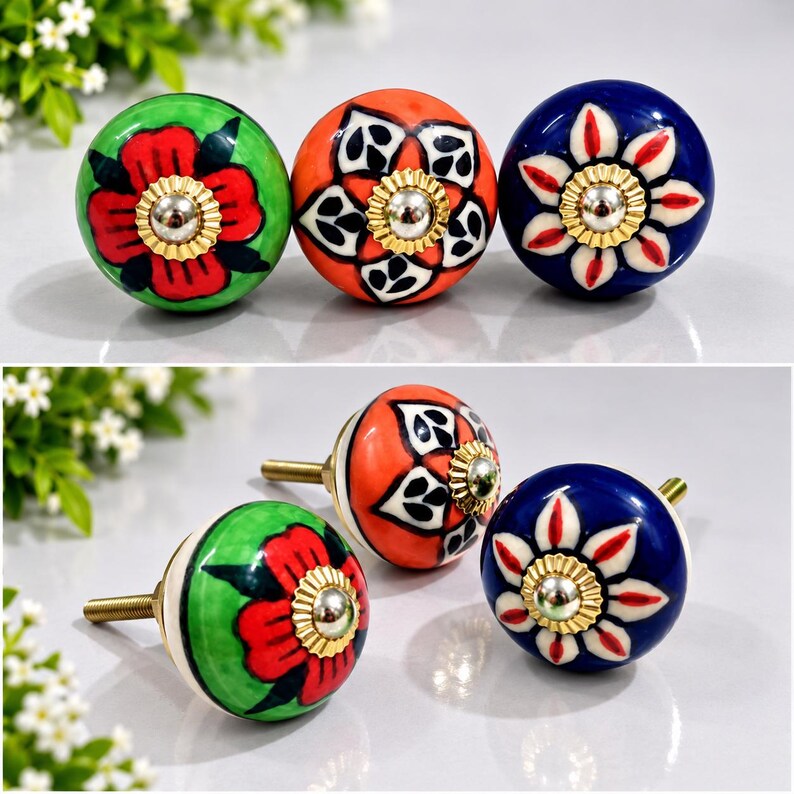 May include: Three round ceramic cabinet knobs featuring hand-painted floral patterns in green, orange, and blue. Each knob has a central gold-toned metal hardware piece with a fluted edge and a threaded metal screw extending from the back.