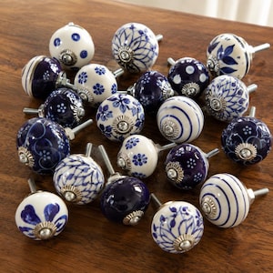 Peut inclure: Une collection de boutons de placard ronds en céramique présentant divers motifs bleus et blancs, notamment des motifs floraux, des rayures, des points et des designs géométriques. Chaque bouton possède une base en métal argenté et une tige filetée.