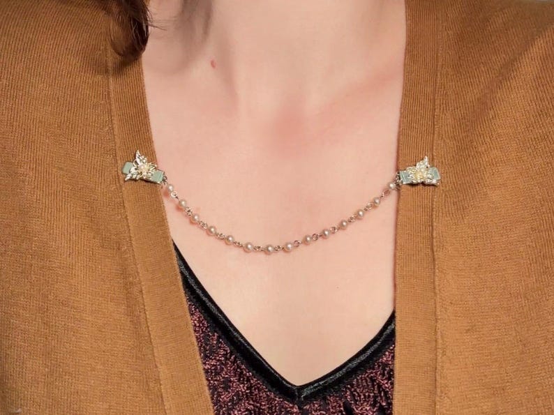 These vintage sweater clips are an absolute treasure. Featuring light gold butterfly clips connected to a cream pearl linked chain. These whimsical butterflies have small alligator clips that gently and securely clip to a cardigan/sweater/jacket/collar, for an instantly elevated look. Sweater clips are a classic vintage accessory popular in the 1940s and 1950s.