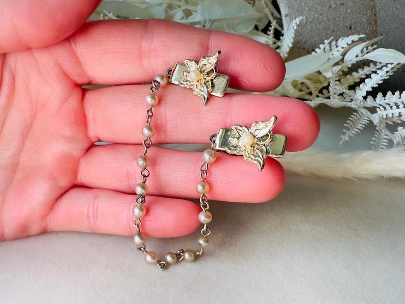 These vintage sweater clips are an absolute treasure. Featuring light gold butterfly clips connected to a cream pearl linked chain. These whimsical butterflies have small alligator clips that gently and securely clip to a cardigan/sweater/jacket/collar, for an instantly elevated look. Sweater clips are a classic vintage accessory popular in the 1940s and 1950s.