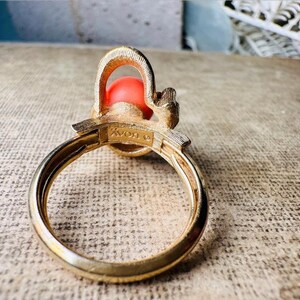 This vintage faux coral and gold Avon ring is a pretty little find. Gold tone ring featuring a vibrant faux coral stone in the center of an intricate gold arch loop. Major abstract space vibes! A unique statement piece by Avon from 1975. Signed in excellent vintage condition. 

Dimensions: US size 6-7 has inner sizer for flexible fit