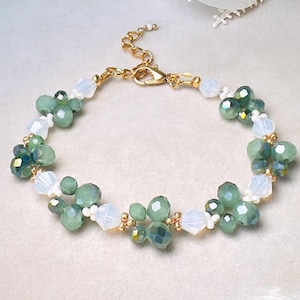 May include: A bracelet featuring clusters of faceted sage green beads alternating with translucent white beads and small gold-toned metal spacers. The piece is finished with a gold-toned metal chain extender and a lobster claw clasp closure.