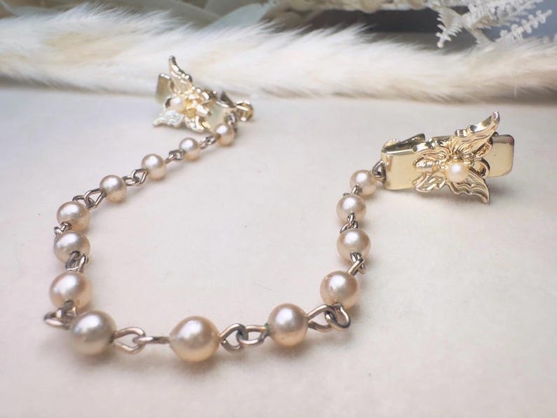 These vintage sweater clips are an absolute treasure. Featuring light gold butterfly clips connected to a cream pearl linked chain. These whimsical butterflies have small alligator clips that gently and securely clip to a cardigan/sweater/jacket/collar, for an instantly elevated look. Sweater clips are a classic vintage accessory popular in the 1940s and 1950s.