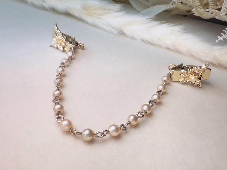 These vintage sweater clips are an absolute treasure. Featuring light gold butterfly clips connected to a cream pearl linked chain. These whimsical butterflies have small alligator clips that gently and securely clip to a cardigan/sweater/jacket/collar, for an instantly elevated look. Sweater clips are a classic vintage accessory popular in the 1940s and 1950s.