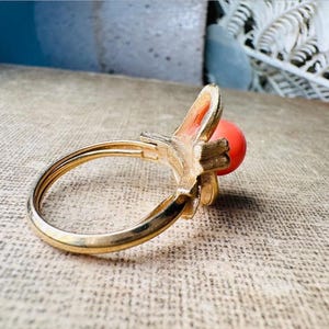 This vintage faux coral and gold Avon ring is a pretty little find. Gold tone ring featuring a vibrant faux coral stone in the center of an intricate gold arch loop. Major abstract space vibes! A unique statement piece by Avon from 1975. Signed in excellent vintage condition. 

Dimensions: US size 6-7 has inner sizer for flexible fit