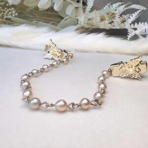 These vintage sweater clips are an absolute treasure. Featuring light gold butterfly clips connected to a cream pearl linked chain. These whimsical butterflies have small alligator clips that gently and securely clip to a cardigan/sweater/jacket/collar, for an instantly elevated look. Sweater clips are a classic vintage accessory popular in the 1940s and 1950s.