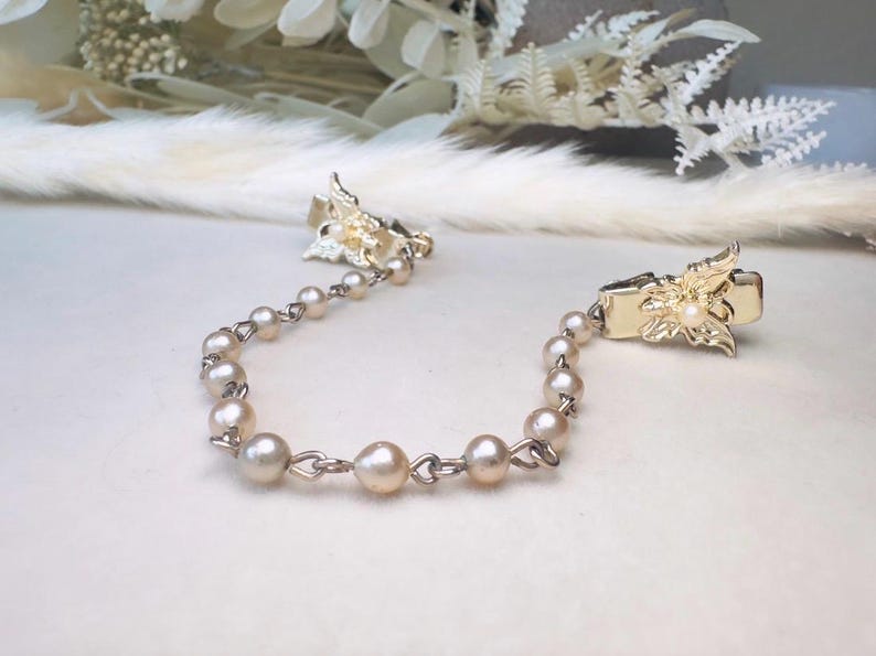 These vintage sweater clips are an absolute treasure. Featuring light gold butterfly clips connected to a cream pearl linked chain. These whimsical butterflies have small alligator clips that gently and securely clip to a cardigan/sweater/jacket/collar, for an instantly elevated look. Sweater clips are a classic vintage accessory popular in the 1940s and 1950s.