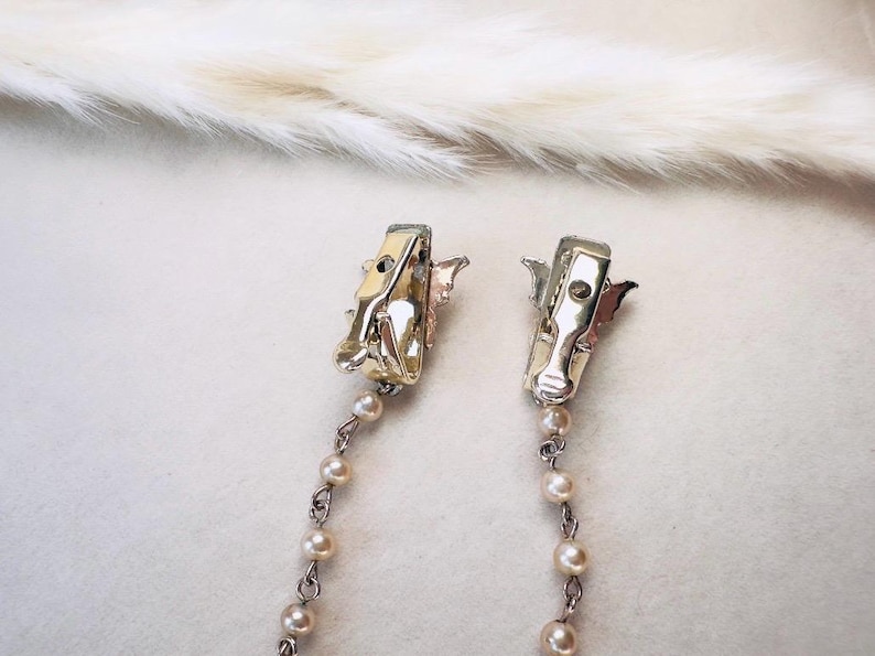 These vintage sweater clips are an absolute treasure. Featuring light gold butterfly clips connected to a cream pearl linked chain. These whimsical butterflies have small alligator clips that gently and securely clip to a cardigan/sweater/jacket/collar, for an instantly elevated look. Sweater clips are a classic vintage accessory popular in the 1940s and 1950s.