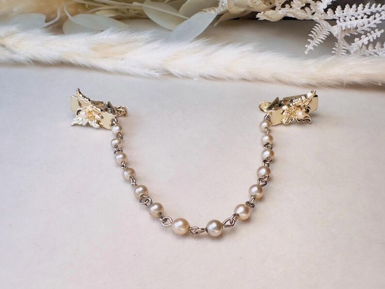 These vintage sweater clips are an absolute treasure. Featuring light gold butterfly clips connected to a cream pearl linked chain. These whimsical butterflies have small alligator clips that gently and securely clip to a cardigan/sweater/jacket/collar, for an instantly elevated look. Sweater clips are a classic vintage accessory popular in the 1940s and 1950s.