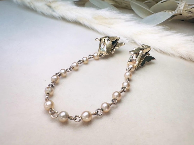 These vintage sweater clips are an absolute treasure. Featuring light gold butterfly clips connected to a cream pearl linked chain. These whimsical butterflies have small alligator clips that gently and securely clip to a cardigan/sweater/jacket/collar, for an instantly elevated look. Sweater clips are a classic vintage accessory popular in the 1940s and 1950s.